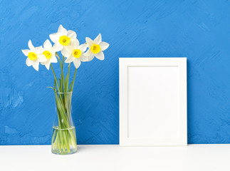 Bouquet of fresh flowers, daffodils in vase on white table, opposite blue textured concrete wall. Empty space for text.