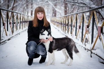 Naklejka na ściany i meble Young beautiful girl playing with siberian husky dog in the winter park