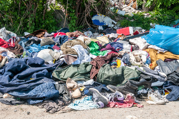 Pile of old clothes and shoes dumped on the grass as junk and garbage, littering and polluting the...