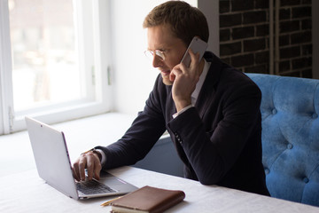 Side view image of businessman sitting at table and talking over phone. Business concept.