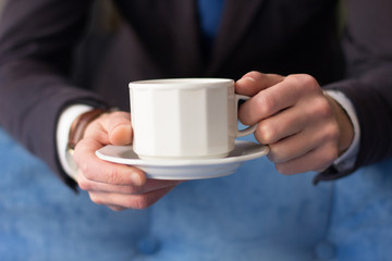 Close up of businessman holding white cup of coffee. Having coffee break.