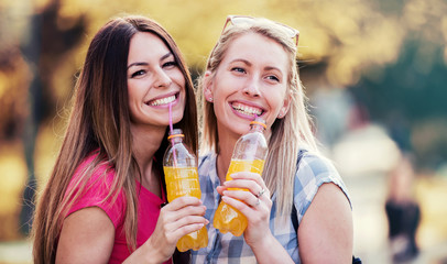 Two smiling girls drinking juice, having fun together in the city. Lifestyle concept