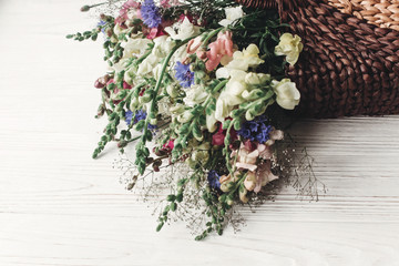 beautiful wildflowers in wicker bag on rustic white wooden background. colorful flowers in basket in light, space for text. rustic wedding concept, woman mothers day, rural summer picture