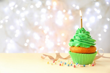 Delicious birthday cupcake with candle on table against blurred background