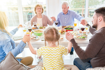 Portrait of big happy family saying grace at dinner holding hands during festive celebration in...