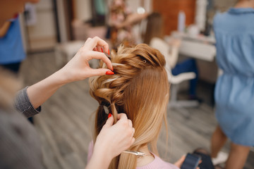 Fototapeta premium Hairdresser woman conducts training for pupil in salon, weaving braid hair, wedding styling.