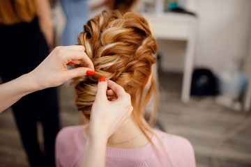 Hairdresser woman conducts training for pupil in salon, weaving braid hair, wedding styling.