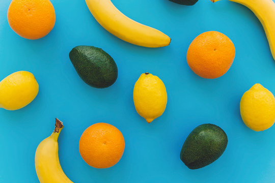 bananas, oranges, lemons, avocado on blue trendy paper background flat lay. summer multi fruit concept, colorful pattern. healthy lifestyle and vacation vibes.