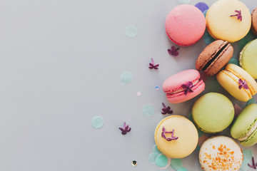 delicious colorful macaroons on trendy pastel gray paper with lilac flowers and confetti, flat lay. tasty pink, yellow, green and brown macaroons. space for text. candy for party