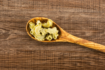 Fototapeta na wymiar Pasta creste di gallo in a wooden olive spoon flatlay spinach raw isolated on brown wood background top view.