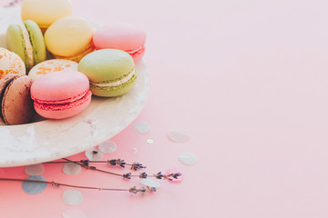 delicious colorful macaroons in vintage white plate on trendy pastel pink paper, modern art image. tasty pink, yellow, green, brown macarons with lavender and confetti. space for text