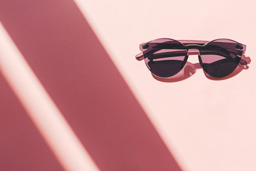 summer vacation and party concept. stylish black sunglasses on trendy pink paper background in sun...