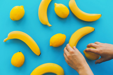 yellow bananas and lemons on blue trendy paper background, flat lay. hands organizing fruits for photo. hand holding banana and lemon. summer concept