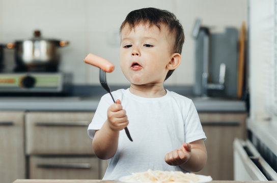 beautiful baby eating sausage with fork and smiling