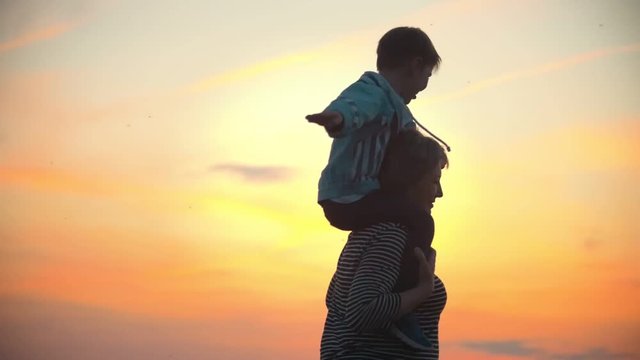 Woman and her children. Child show the plane with their hands. Mother and her little son have fun against the scarlet sunset Mother holds child on shoulders they're spinning.