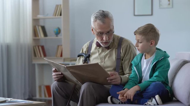 Old man reading book aloud to grandson, giving experience to younger generation