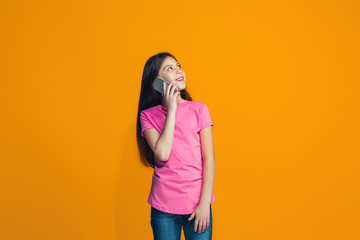 The happy teen girl standing and smiling against orange background.