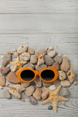 Sunglasses orange color and shells, sea stones and a starfish on the gray wooden background.