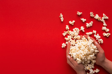 Fototapeta na wymiar Heap of popcorn in hands on red background, top view