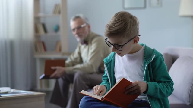 Smart kid in eyeglasses reading book aloud, grandfather feels proud of boy