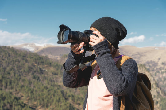 Close-up portrait of a blond girl with a digital SLR camera photographing in the mountains. Stylish freelancer photographer with backpack in mountain caucasian trip