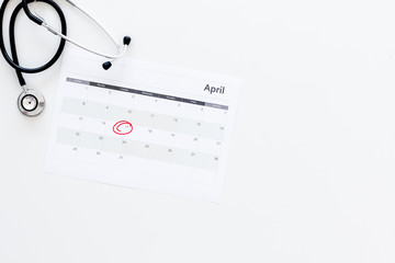 Planning medical examination concept. Regular medical examinations. Calendar with date circled and stethoscope on white background top view copy space