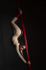 Obraz na płótnie Canvas Joven bailarina realizando ejercicios de telas acrobáticas en estudio con fondo negro