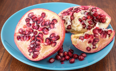 Fresh ripe pomegranate halves on turquoise plate againt brown wooden background, pomegranate seeds