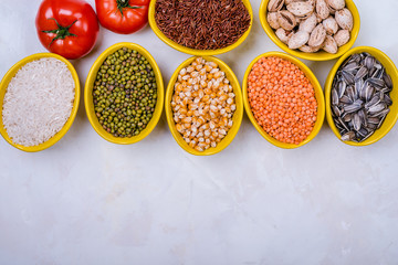Assorted cereals, beans, seeds  in  bowls  on  white concrete table, flat-lay