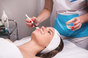 Obraz na płótnie Canvas Stunning young woman with hair fixed behind,clean fresh skin naked shoulders wearing white bath robe and hair wrap, doing cosmetic procedure, close up, microdermabrasion