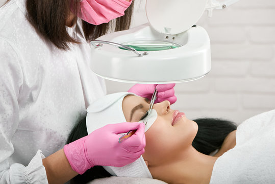 Professional working with a client in beaty salon. Woman lying on cosmetologiacal coach during lashes enlarging. Model with pretty face wearing headbandage and stickers for lashmaking .