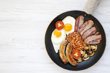 Top view, full English Breakfast in cooking pan with sausages, fried eggs, beans and bacon on a white wooden background. Copy space. Flat lay. From above.