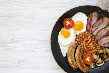 Full English Breakfast in cooking pan with sausages, mushrooms, fried eggs, beans, tomatoes and bacon on a white wooden background. Top view. Copy space. Flat lay. From above.