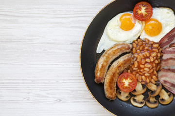Full English Breakfast in cooking pan with sausages, mushrooms, fried eggs, beans, tomato and bacon on a white wooden background with copy space. Top view. Flat lay. From above.