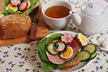 parsley dill boiled egg and flower radish cucumber and ham on fresh bread tea in a cup for breakfast