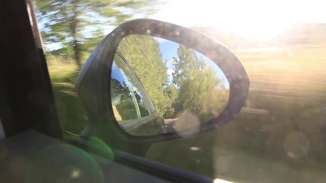 Traveling desde coche con el retrovisor derecho reflejando el sol y paisaje de atardecer

