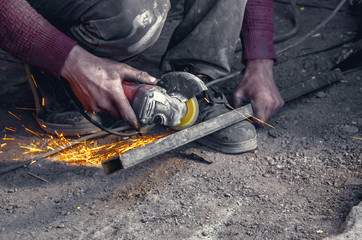 Manual cutting metal pipe with a circular saw. Hands, worker, flying sparks. - obrazy, fototapety, plakaty