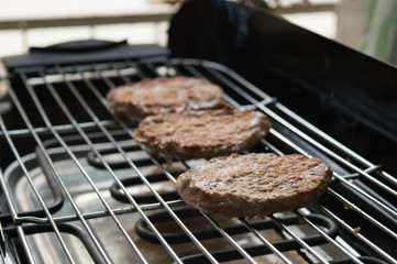 Three tasty meat hamburgers cooking on electric grill. A nice day to cook at the backyard