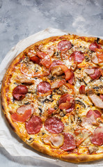 Fresh homemade pizza with pepperoni, ham, cheese and tomato sauce on rustic concrete background