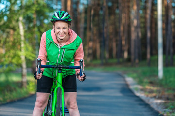 Girl on a racing bike in the park. Green vest, bicycle and green helmet. A happy face. Doing sports.