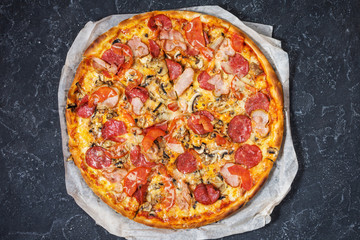 Fresh homemade pizza with pepperoni, ham, cheese and tomato sauce on rustic stone background