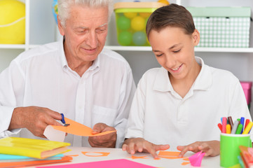 Grandfather and grandson gluing and cutting colorful paper