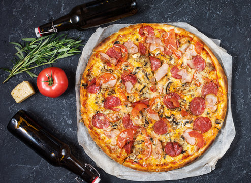 Fresh Homemade Pizza With Pepperoni, Ham, Cheese And Bottle Of Beer On Rustic Stone Background