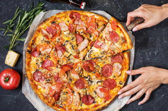 Female hands hold a piece Fresh homemade pizza with pepperoni, ham, cheese on rustic stone background