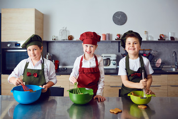 A group of children preparing a dough at the table in the kitchen.