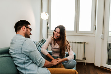 Cute couple holding hands while talking on sofa.