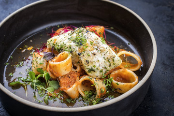 braised codfish filet and lettuce, herbs with calamarata noodles as top view on a plate
