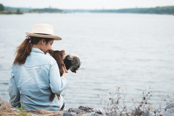 Happy young asian woman sitting with her dog beside reservoir.