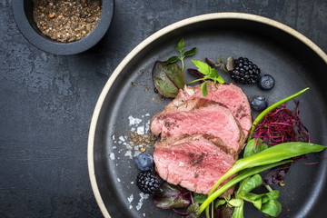 Traditionelles gegrilltes gereiftes Filet Steak aufgeschnitten mit Bärlauch und Früchten als Draufsicht auf Teller mit Textfreiraum links