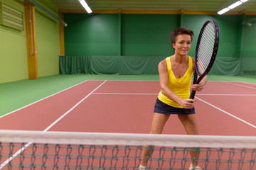 Mature beautiful woman playing tennis at indoor court